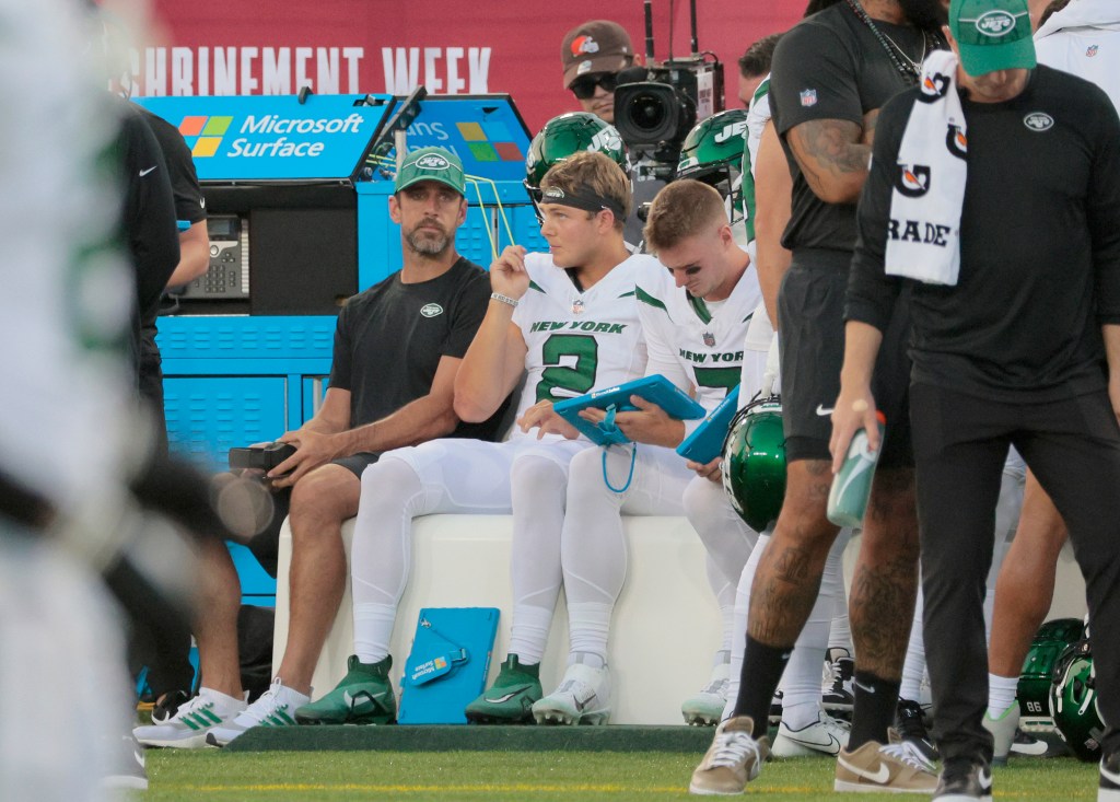 Aaron Rodgers and Zach Wilson talk on the bench during a Jets preseason game.