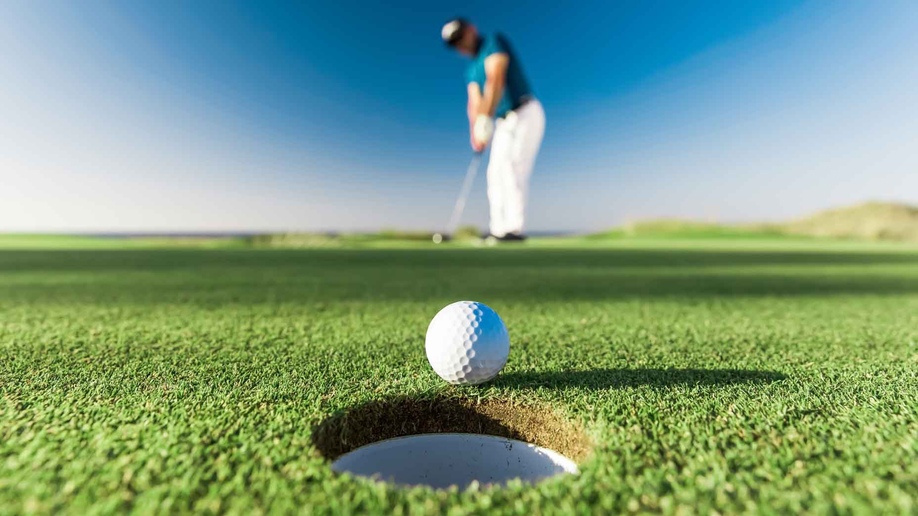 a golfer putts a golf ball into a hole from a long distance on a golf course