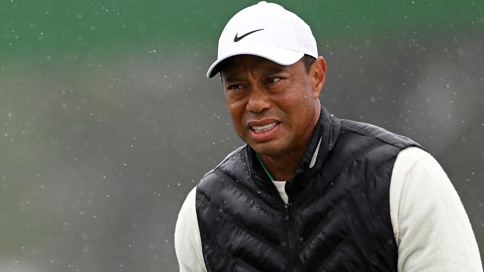 Tiger Woods walks in the rain at the Masters tournament in a white hat.